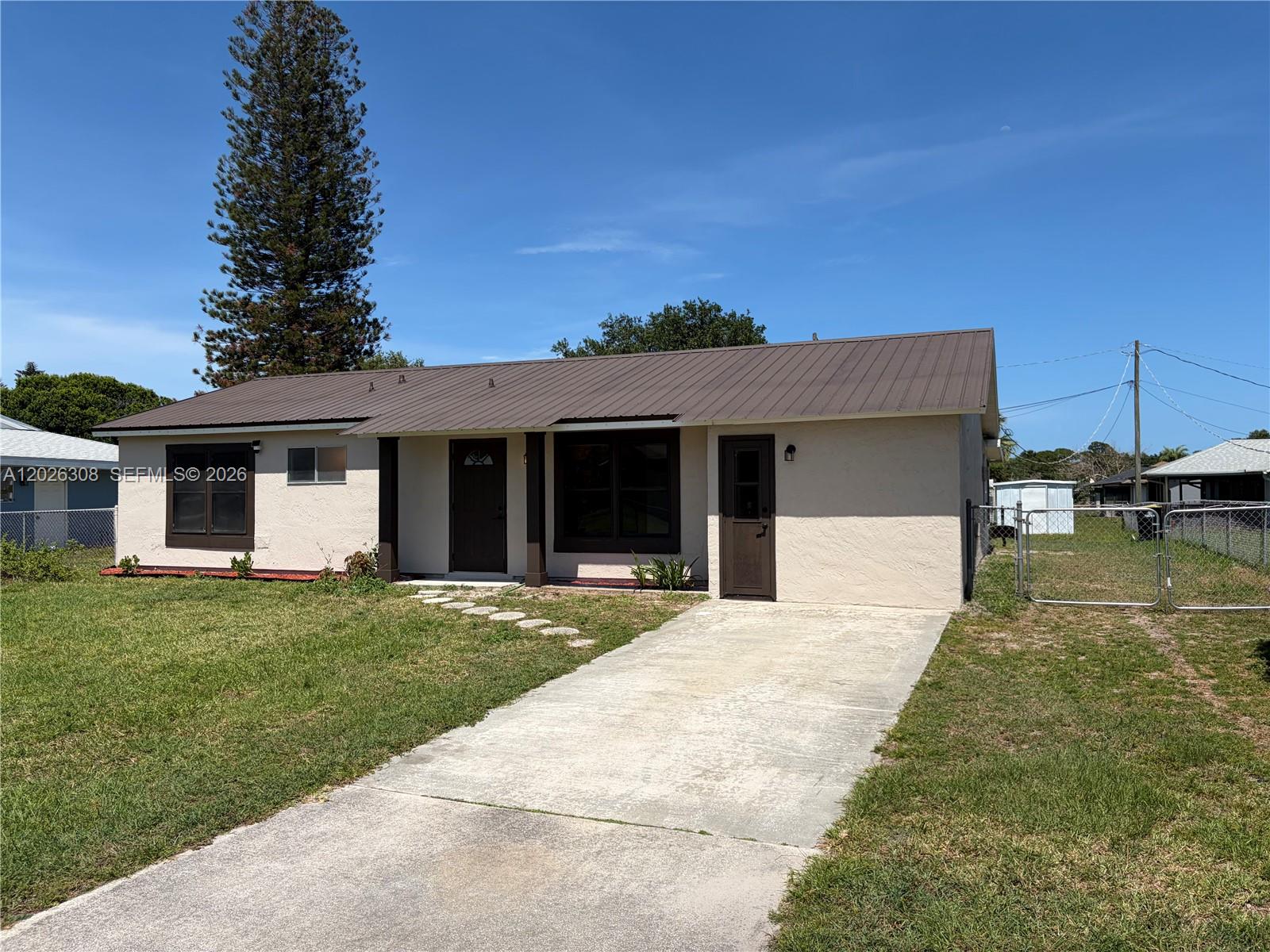 A single-story house with a brown metal roof, beige stucco exterior, and a concrete driveway — 653 NE Atlas Avenue, Palm Bay FL 32905, PALM BAY, FL