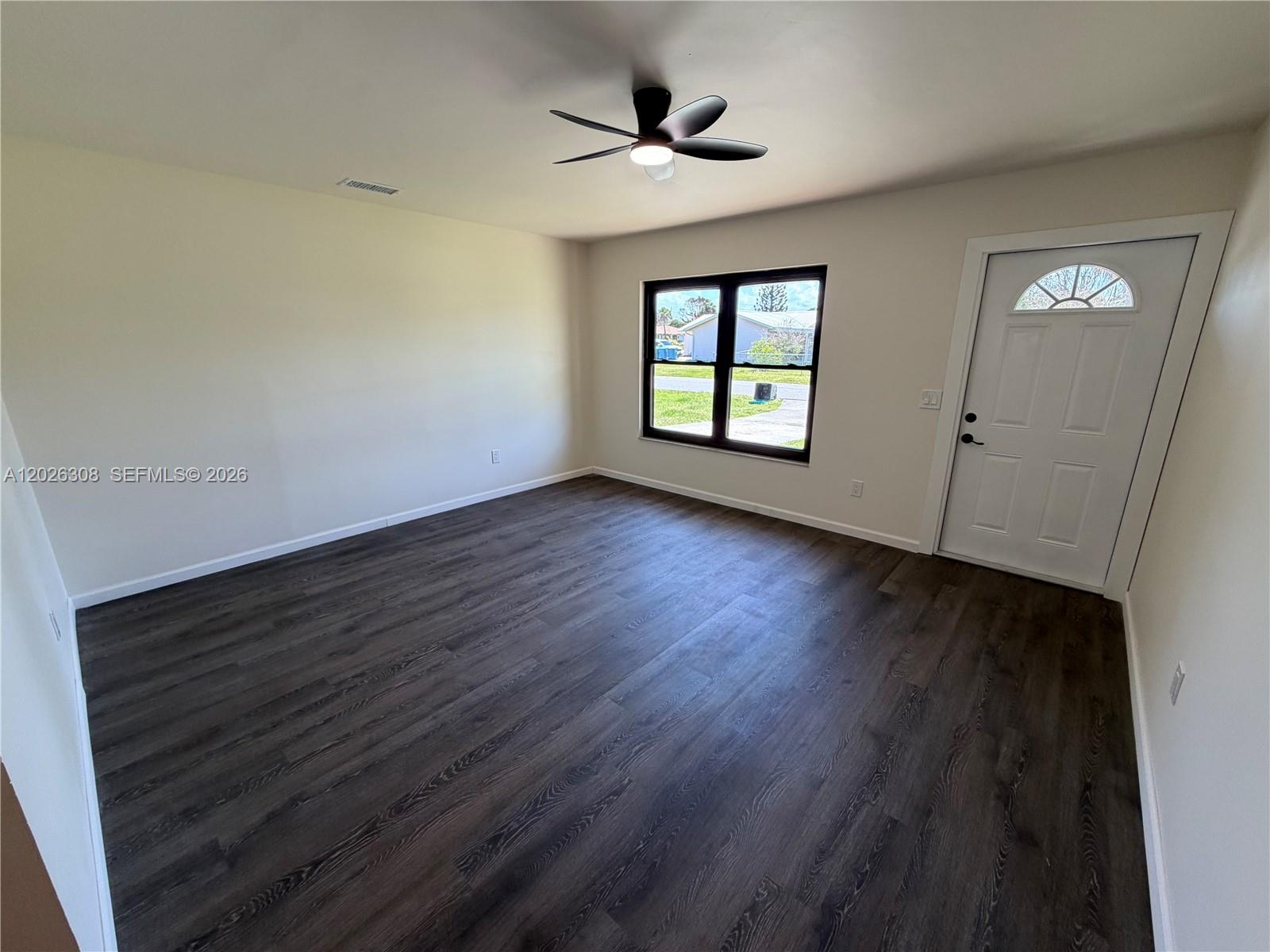 An empty room features dark wood-look flooring, a ceiling fan, and a white entry door — 653 NE Atlas Avenue, Palm Bay FL 32905, PALM BAY, FL