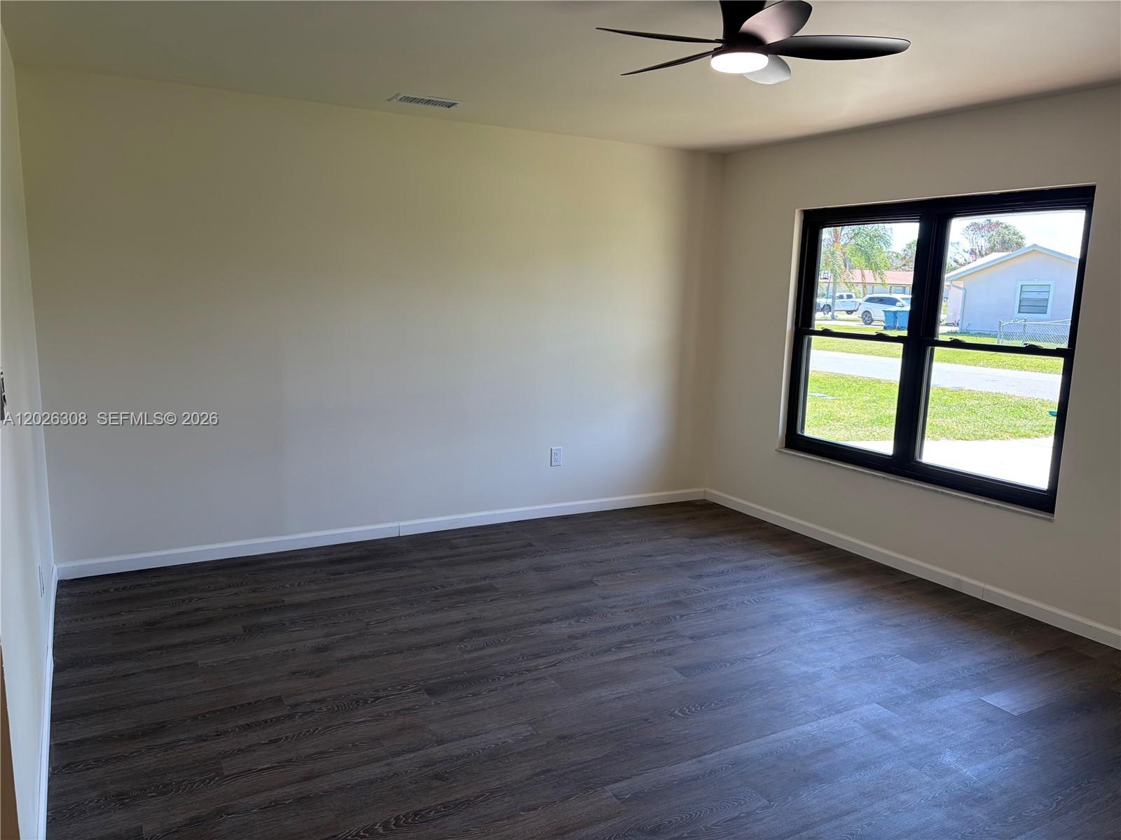 An empty room features dark wood-look flooring, light-colored walls, a ceiling fan, and a window — 653 NE Atlas Avenue, Palm Bay FL 32905, PALM BAY, FL