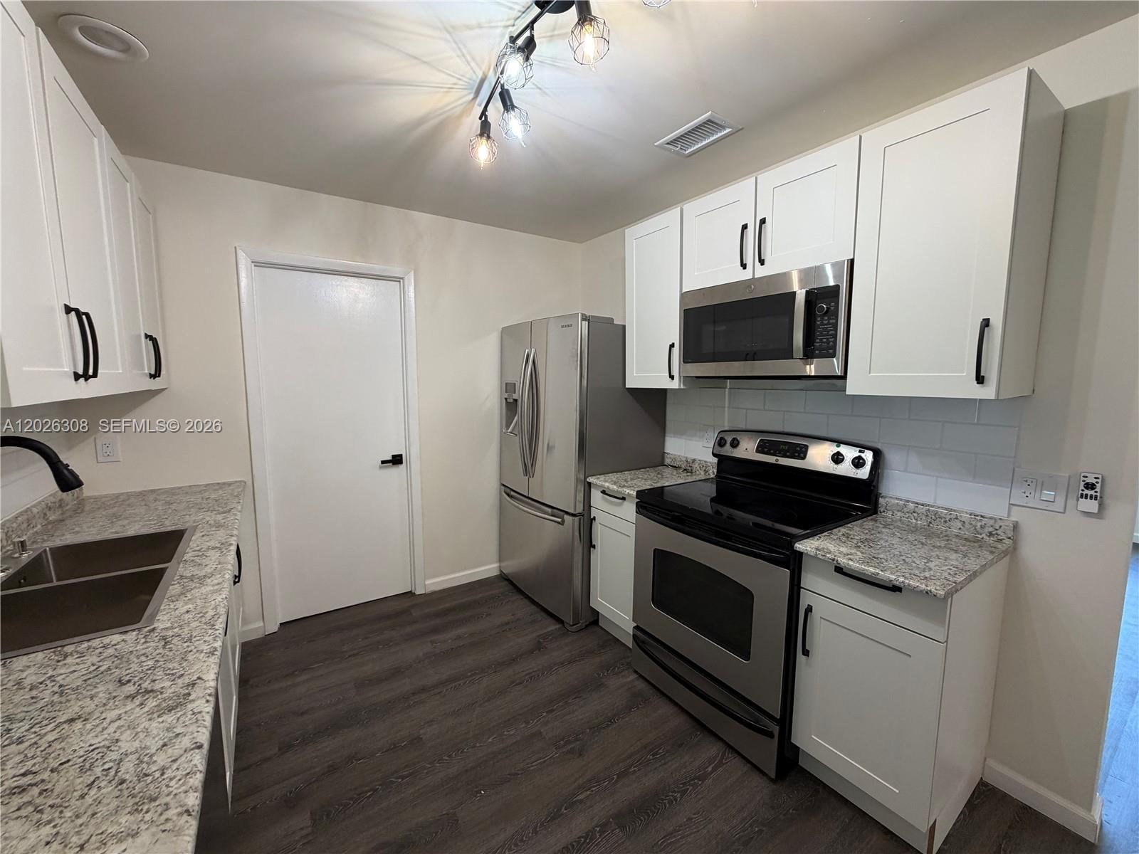 A kitchen features white cabinets, stainless steel appliances, granite countertops, and dark wood-look flooring — 653 NE Atlas Avenue, Palm Bay FL 32905, PALM BAY, FL