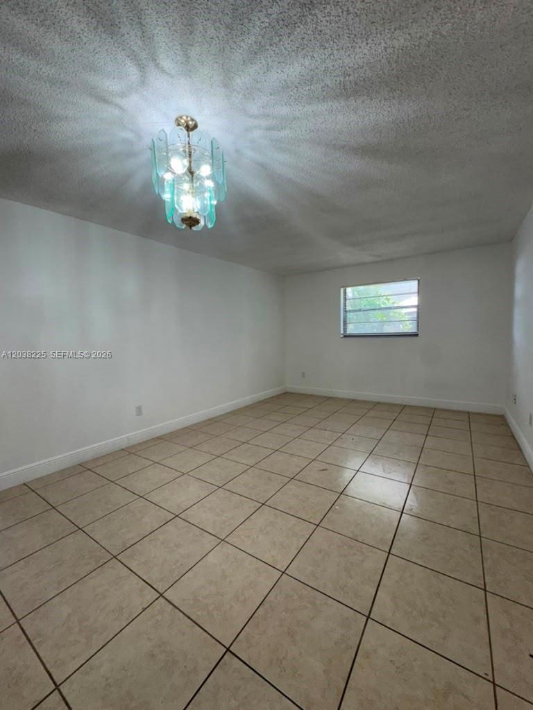 An empty room features white walls, tan tile flooring, and a decorative glass chandelier — HIALEAH, FL