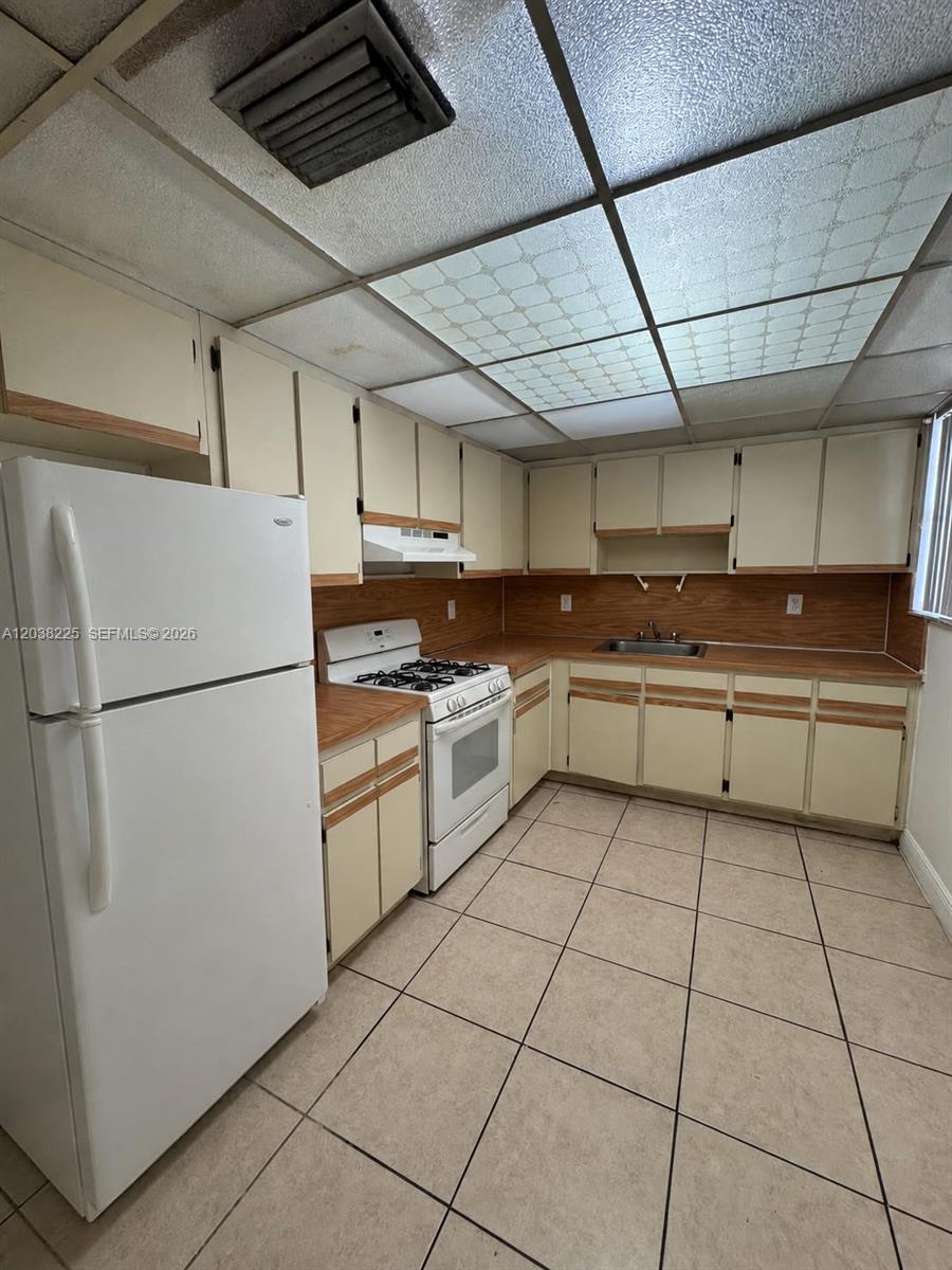 A kitchen features beige cabinets, wood-look countertops, white appliances, and a drop ceiling — HIALEAH, FL