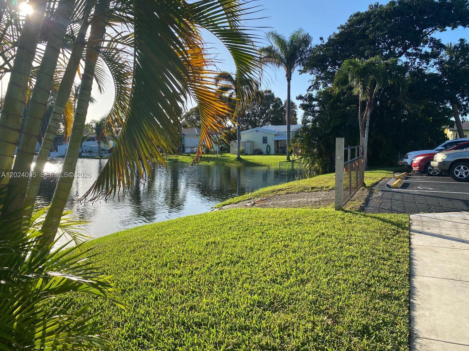 A grassy lawn leads to a small pond with palm trees and a parking area — HOLLYWOOD, FL