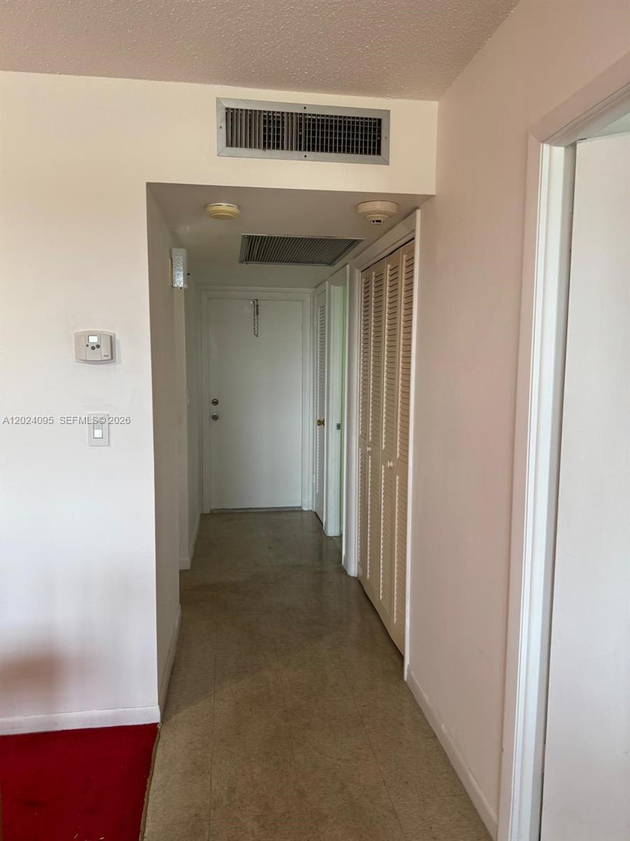 A hallway with beige flooring leads to a white door and a louvered closet — HOLLYWOOD, FL