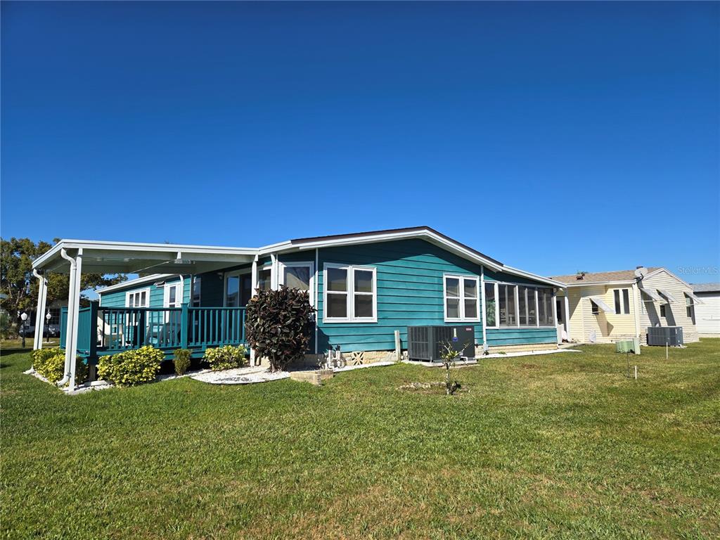 A teal manufactured home with a covered deck and a large lawn under a blue sky — 312 TOWNBRIDGE DRIVE, HAINES CITY, FL