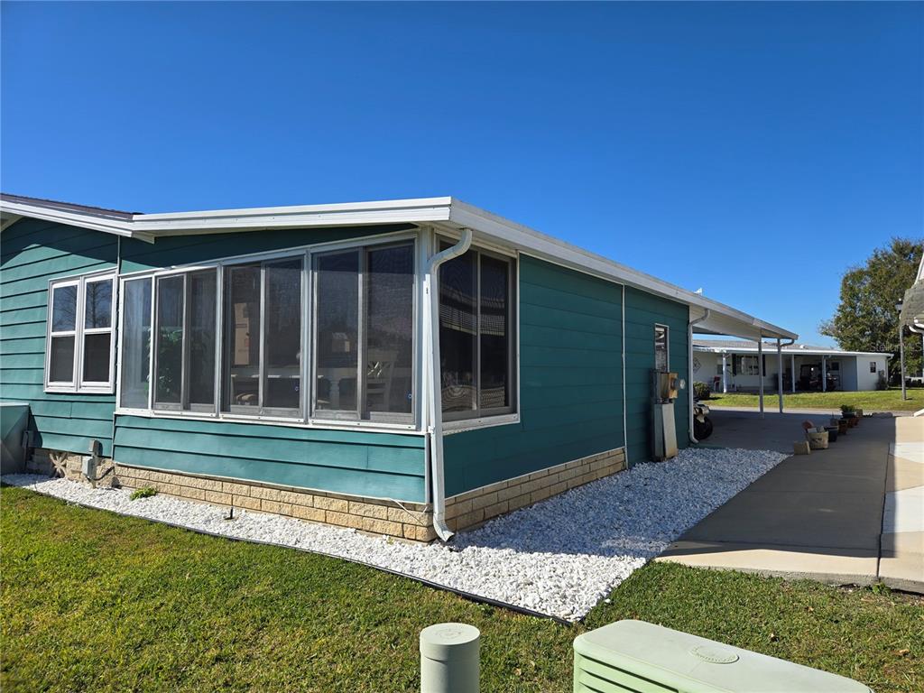 A teal mobile home features a screened-in porch, a carport, and a white gravel landscape — 312 TOWNBRIDGE DRIVE, HAINES CITY, FL