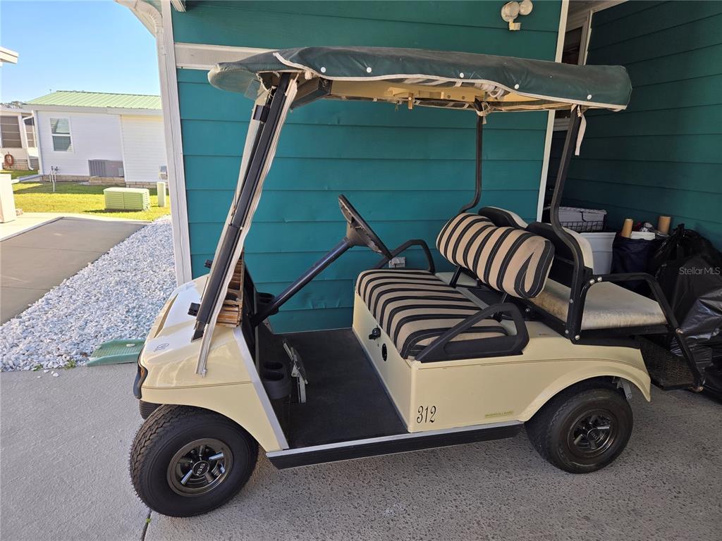 A cream-colored golf cart with striped seats is parked on a concrete patio — 312 TOWNBRIDGE DRIVE, HAINES CITY, FL