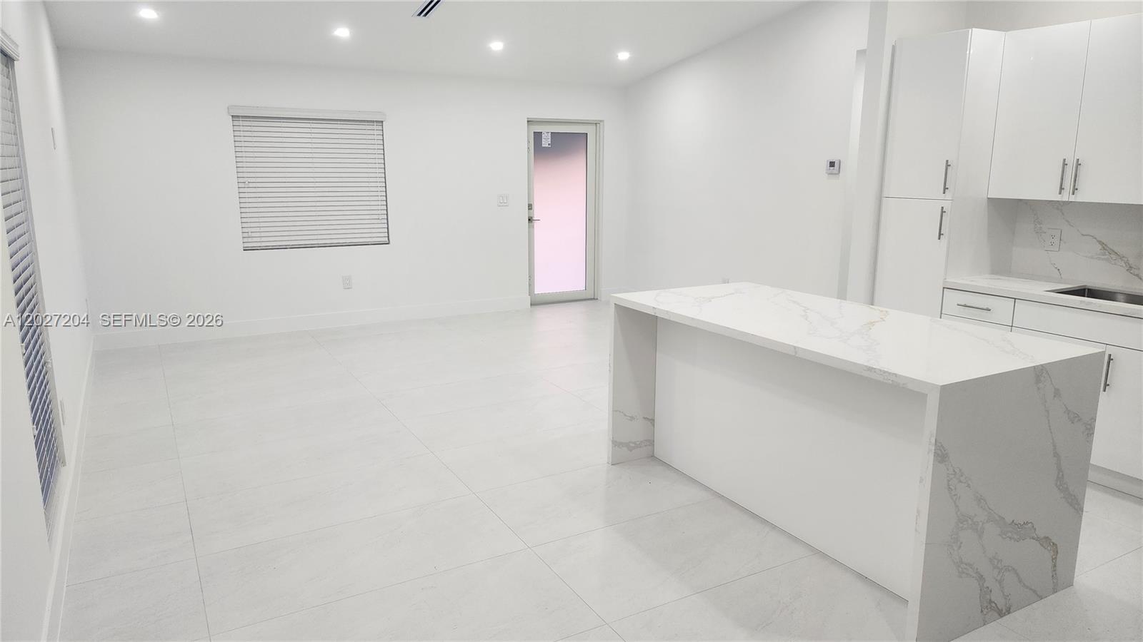 A modern kitchen and living area feature white cabinetry, marble-patterned countertops, and light tile flooring — 13741 SW 46th Ter, Miami FL 33175, MIAMI, FL