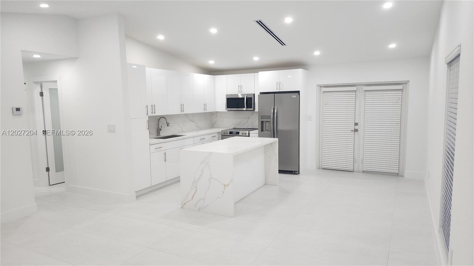 A modern white kitchen features a marble-topped island, stainless steel appliances, and tile flooring — 13741 SW 46th Ter, Miami FL 33175, MIAMI, FL