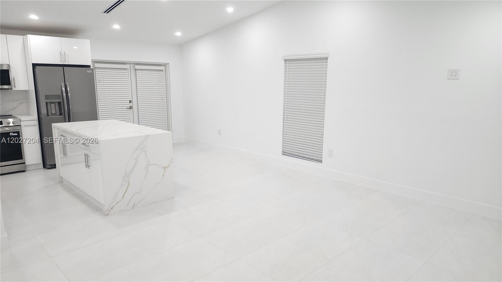 A modern kitchen features white cabinets, a marble-topped island, and light-colored tile flooring — 13741 SW 46th Ter, Miami FL 33175, MIAMI, FL