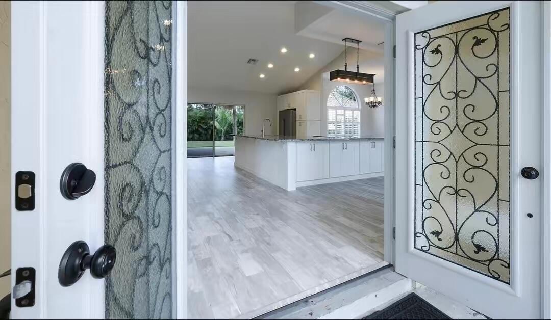 A view through open front doors into a kitchen with white cabinets and wood flooring — 13383 Temple Boulevard, West Palm Beach FL 33412, WEST PALM BEACH, FL