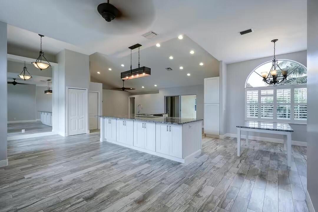 A bright kitchen features a white island, granite countertops, wood-look tile flooring, and recessed lighting — 13383 Temple Boulevard, West Palm Beach FL 33412, WEST PALM BEACH, FL