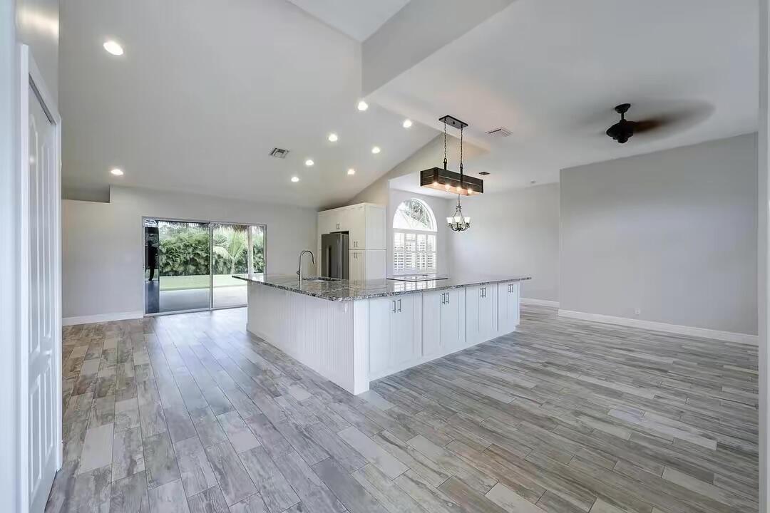 A spacious kitchen features a large white island with granite countertops and wood-look tile flooring — 13383 Temple Boulevard, West Palm Beach FL 33412, WEST PALM BEACH, FL