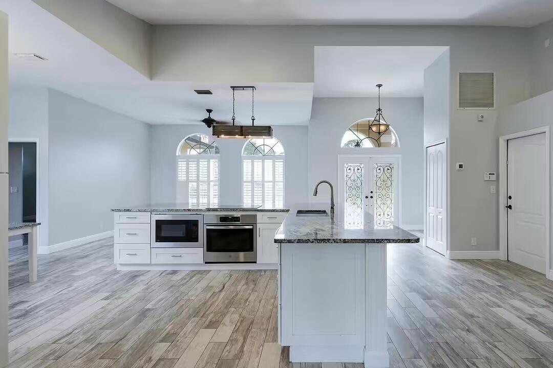A modern kitchen features white cabinetry, granite countertops, stainless steel appliances, and wood-look tile flooring — 13383 Temple Boulevard, West Palm Beach FL 33412, WEST PALM BEACH, FL