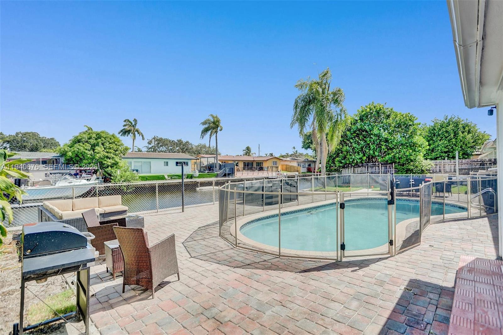 A backyard patio features a swimming pool with a safety fence, furniture, and canal views — 2827 Arthur St, Hollywood FL 33020, HOLLYWOOD, FL