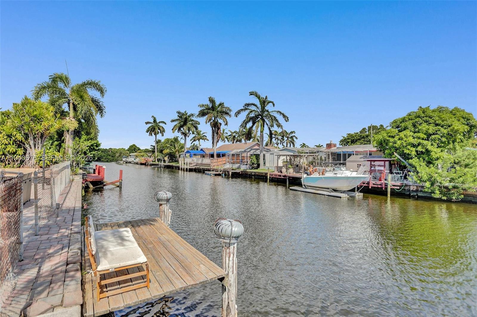 A wooden dock with a bench overlooks a canal lined with houses and palm trees — 2827 Arthur St, Hollywood FL 33020, HOLLYWOOD, FL