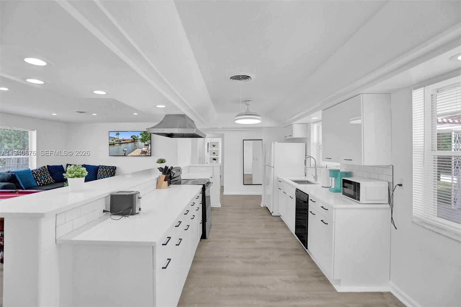 A modern white kitchen features a long island, stainless steel appliances, and light wood flooring — 2827 Arthur St, Hollywood FL 33020, HOLLYWOOD, FL