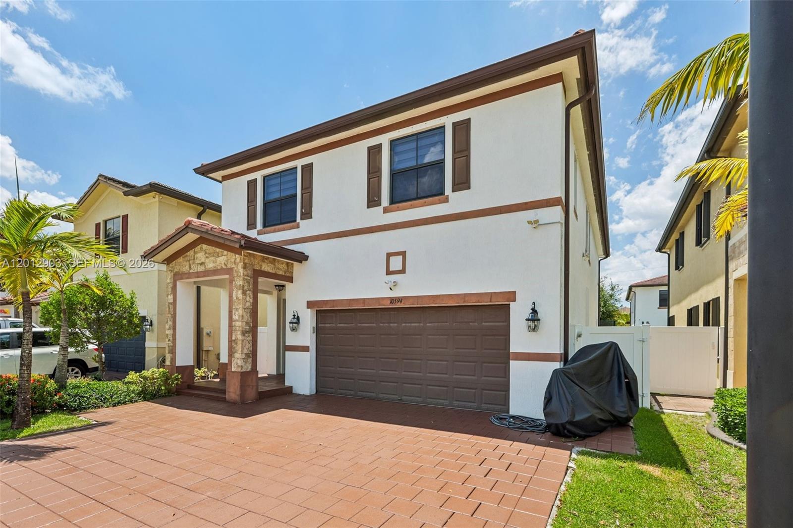 A two-story house with a brown garage door, stone-accented entryway, and paved driveway — 10594 W 35th Ln, Hialeah FL 33018, HIALEAH, FL