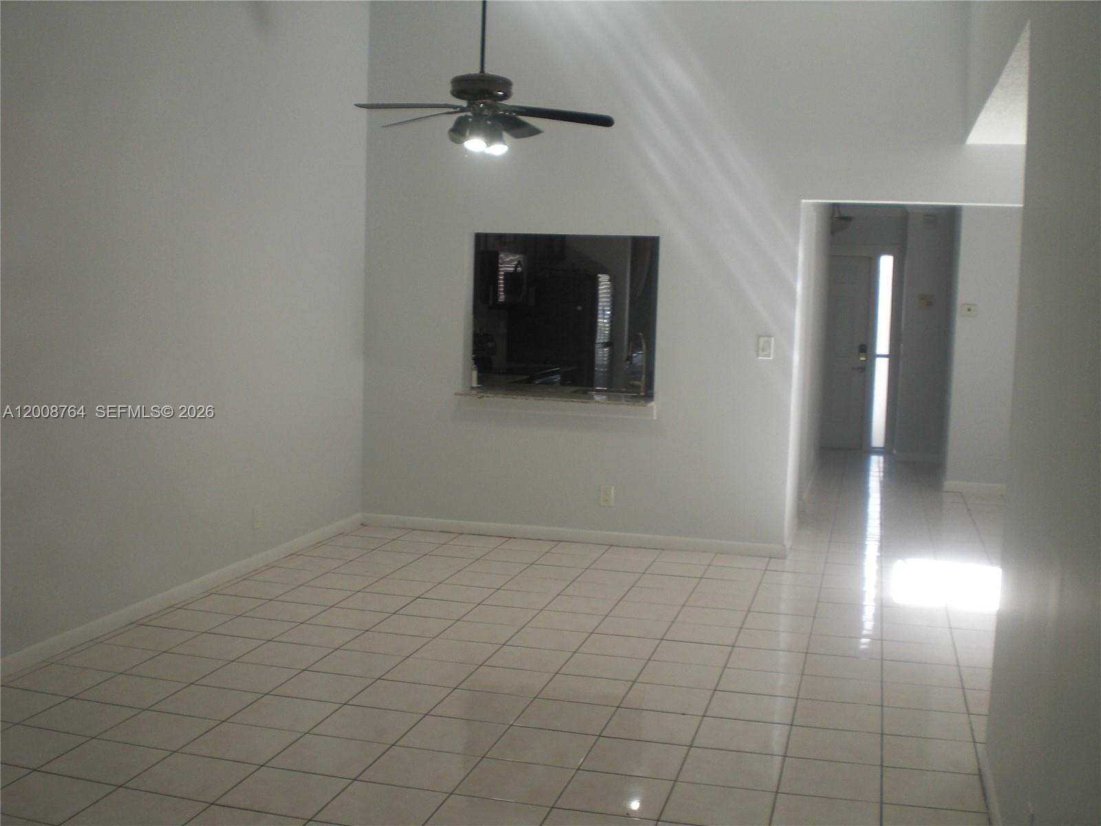 An empty room features white tile floors, a ceiling fan, and a kitchen pass-through window — 962 NW 79th Ter, Plantation FL 33324, PLANTATION, FL