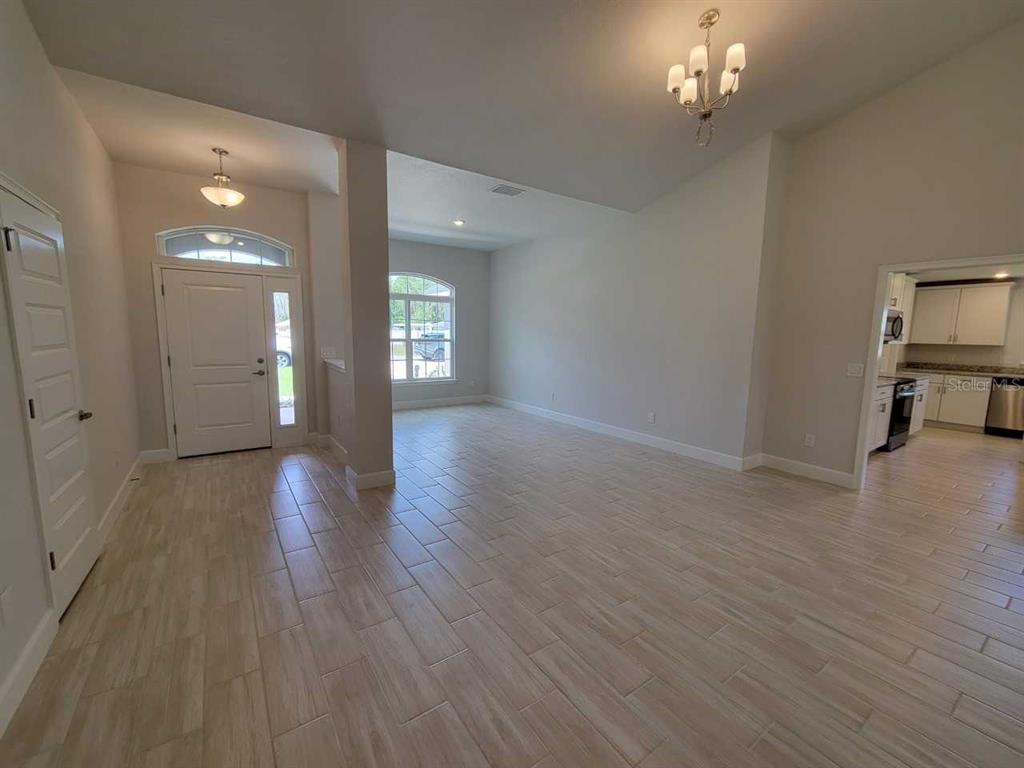 A spacious room with light-colored wood-look tile flooring, vaulted ceilings, and a central chandelier — 12598 SW 73RD STREET, OCALA, FL
