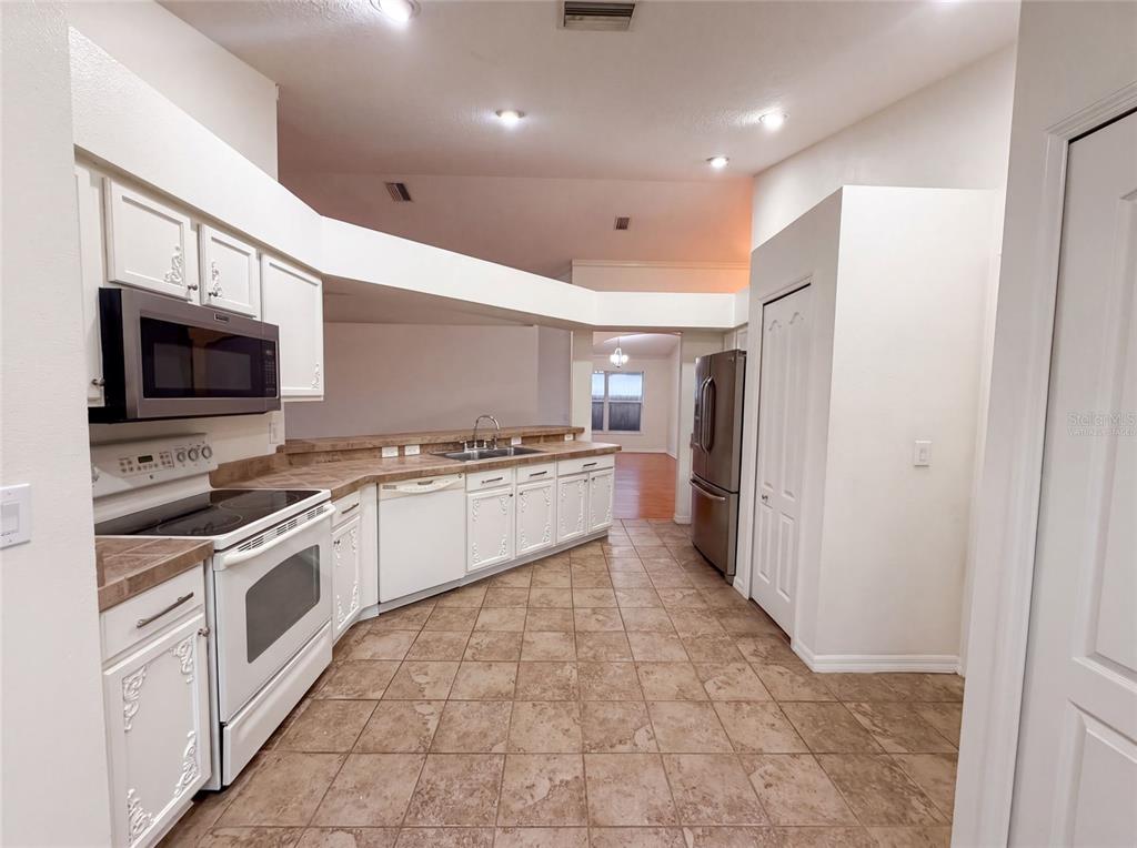 A kitchen features white cabinets, stainless steel appliances, tile flooring, and a brown laminate countertop — 6941 CROWN LAKE DRIVE, GIBSONTON, FL