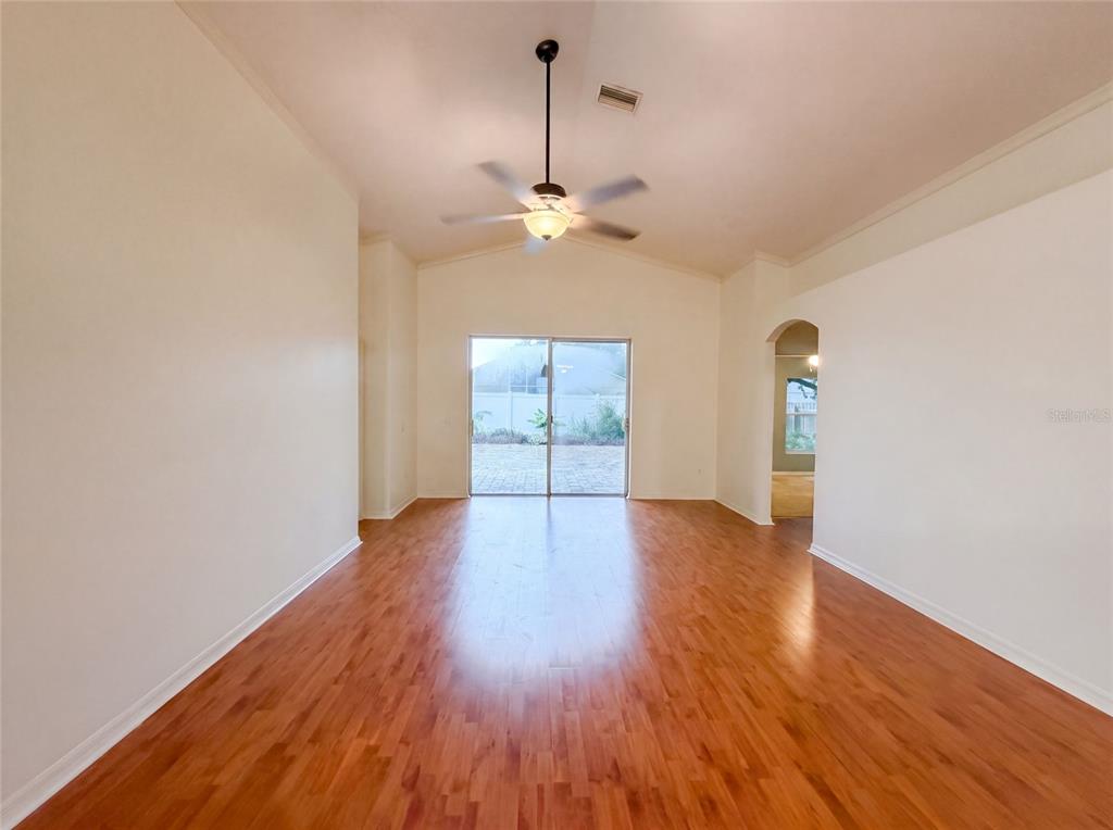 An empty living room features wood-look flooring, a vaulted ceiling with a fan, and sliding doors — 6941 CROWN LAKE DRIVE, GIBSONTON, FL