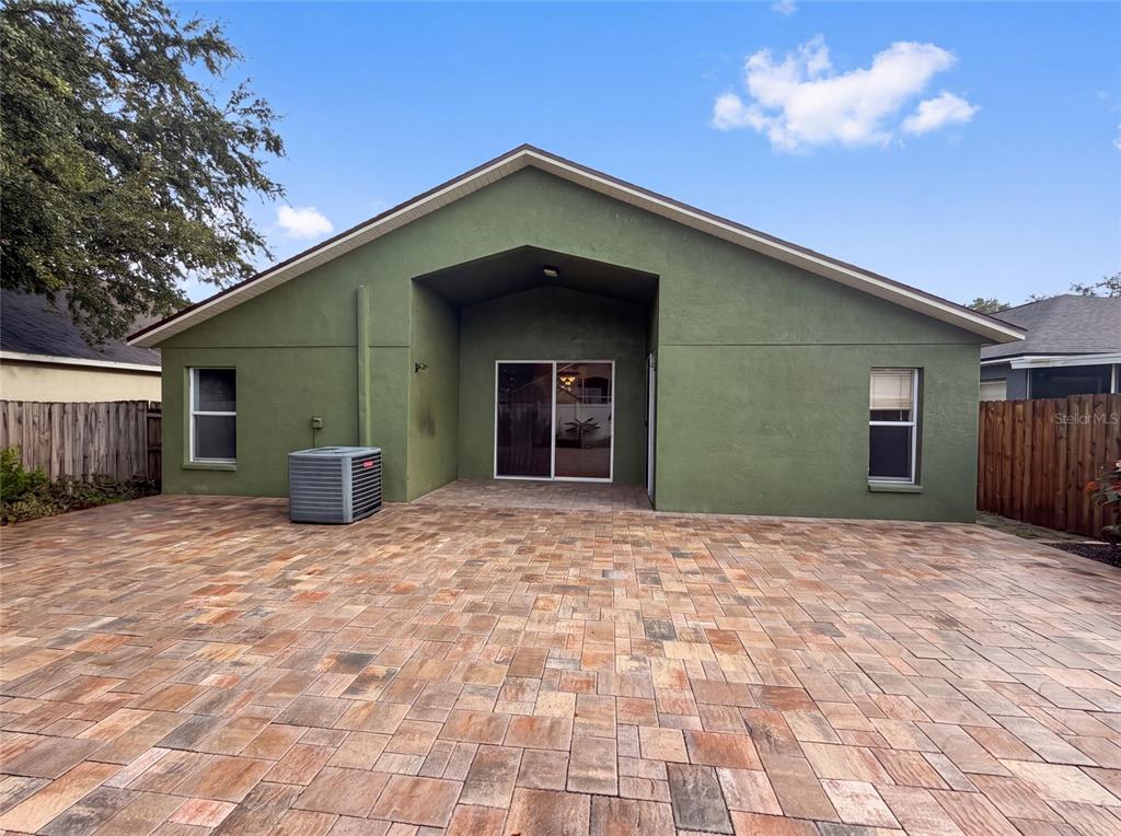 The exterior of a green house features a large paved patio and a sliding glass door — 6941 CROWN LAKE DRIVE, GIBSONTON, FL