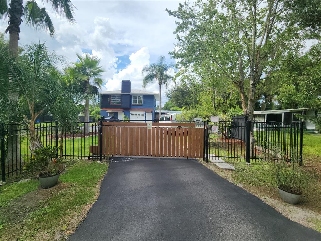 A gated driveway leads to a two-story blue house surrounded by trees and palm trees — 5113 PALMETTO ROAD, KISSIMMEE, FL