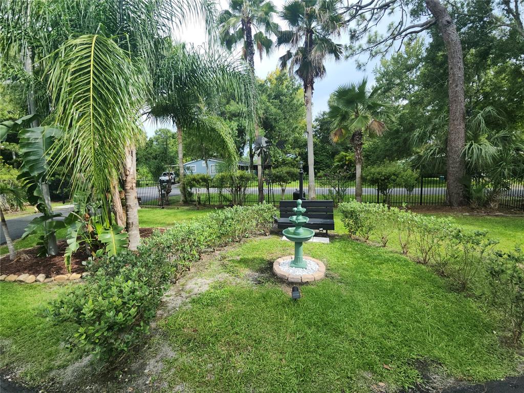 A green tiered fountain sits in a grassy yard with palm trees and a bench — 5113 PALMETTO ROAD, KISSIMMEE, FL