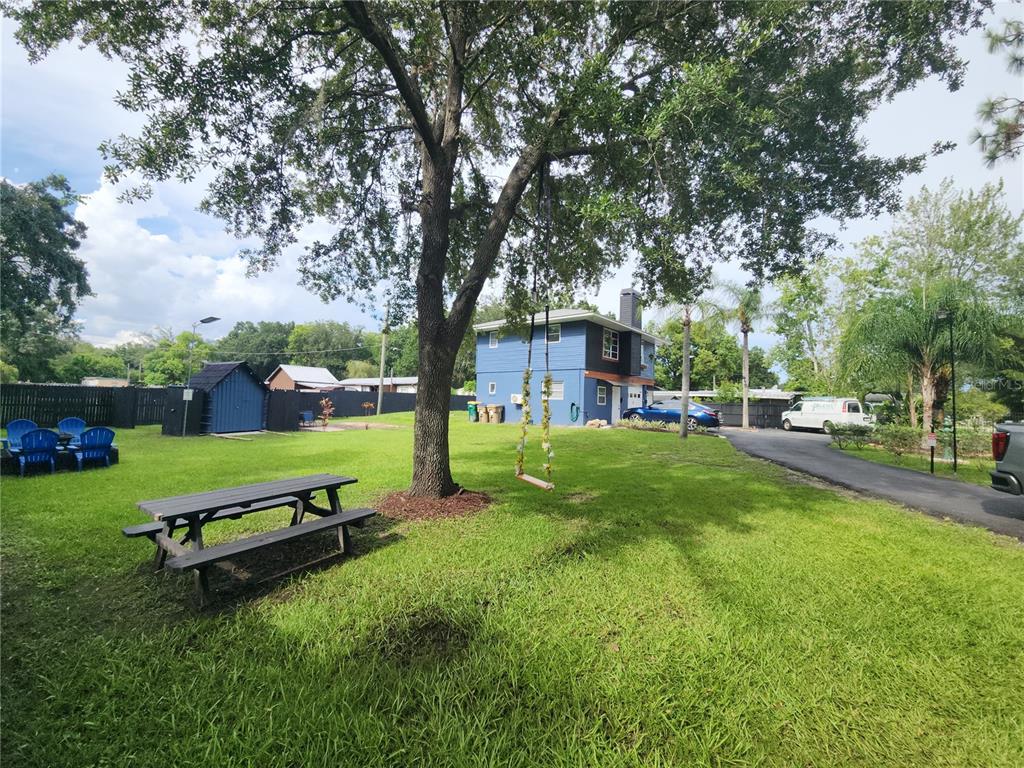 A large backyard features a picnic table, a tree swing, and a blue two-story house — 5113 PALMETTO ROAD, KISSIMMEE, FL