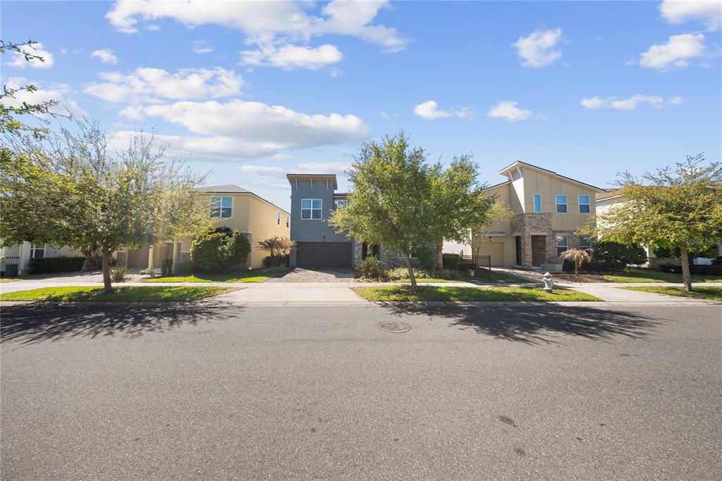 A street view of three modern suburban houses with driveways and trees under a blue sky — 9014 PELICAN COVE TRAIL, KISSIMMEE, FL