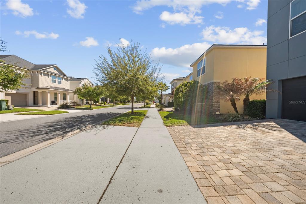 A paved street runs between residential houses with sidewalks and trees under a blue sky — 9014 PELICAN COVE TRAIL, KISSIMMEE, FL
