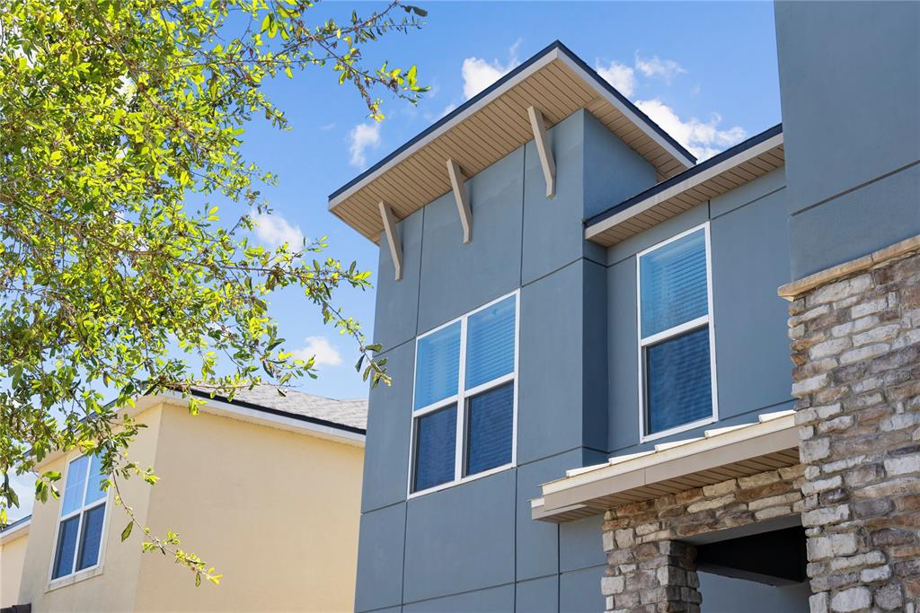 A low-angle view of a blue modern home exterior with stone accents and two windows — 9014 PELICAN COVE TRAIL, KISSIMMEE, FL