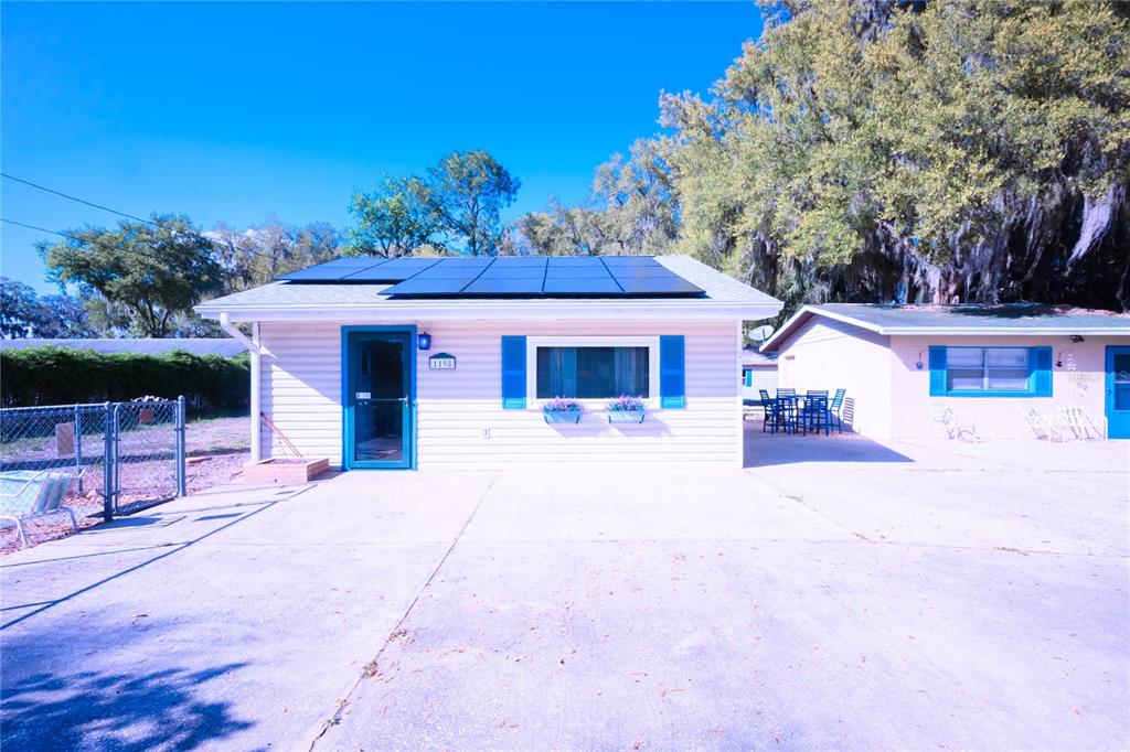 A single-story house with light siding, blue shutters, and solar panels on the roof — 1198 CR 464, LAKE PANASOFFKEE, FL