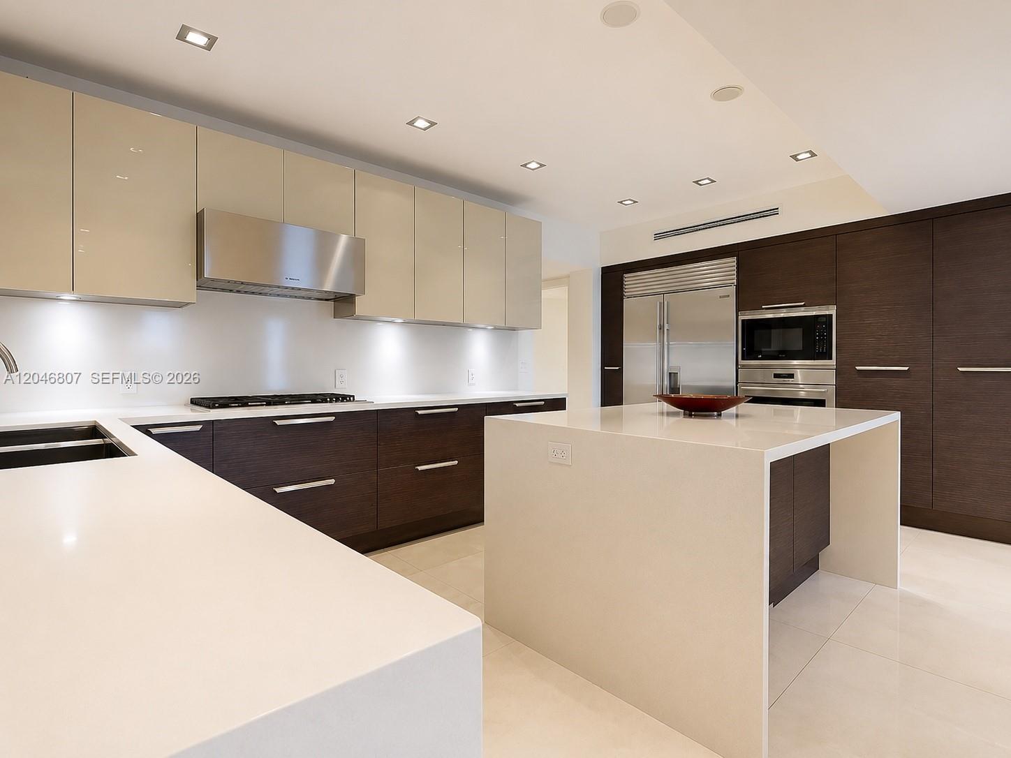 A modern kitchen features two-toned cabinetry, a large white waterfall island, and stainless steel appliances — 260 S Coconut Ln, Miami Beach FL 33139, MIAMI BEACH, FL