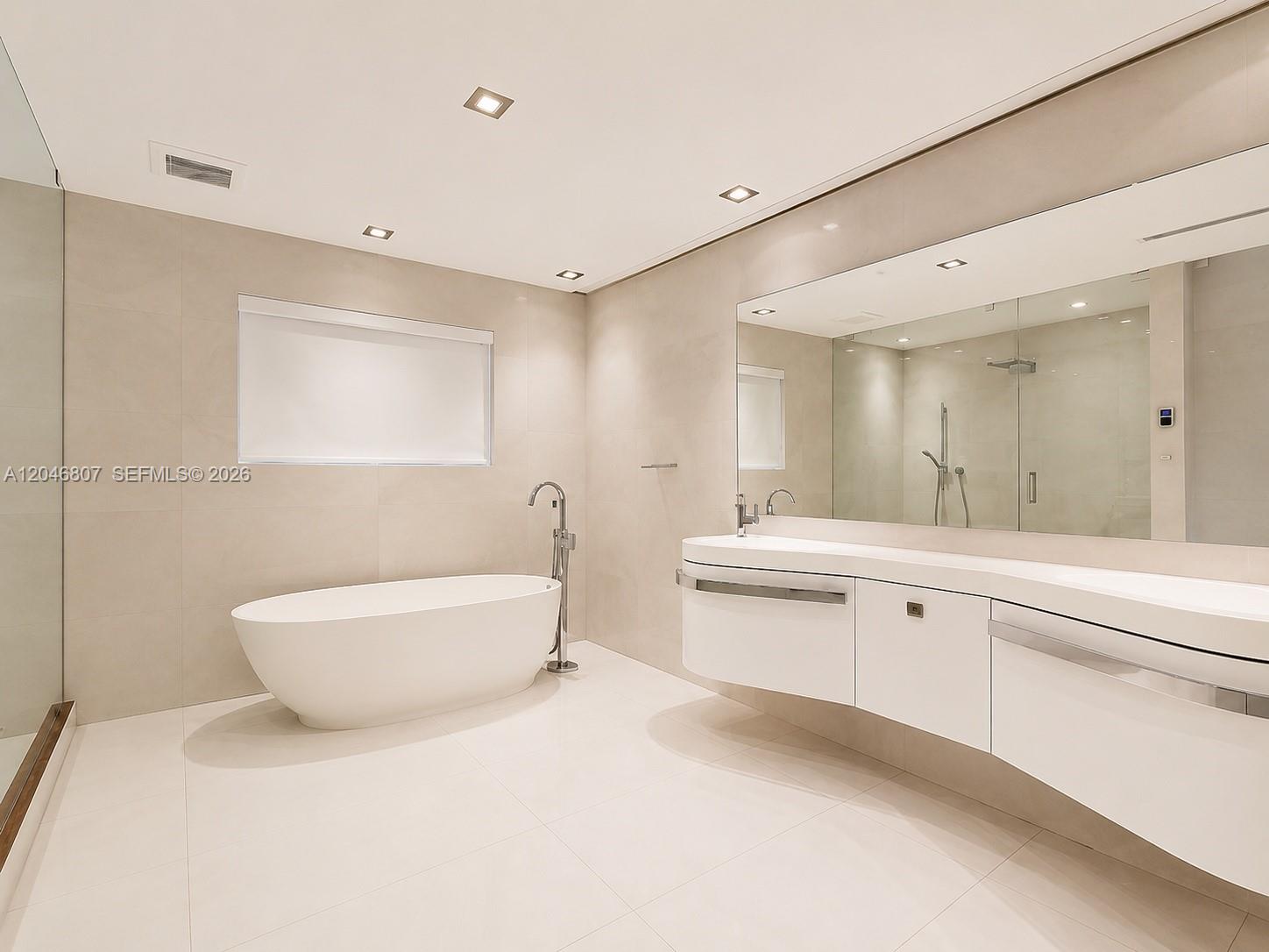 A modern bathroom features a freestanding tub, a floating vanity, and large beige wall tiles — 260 S Coconut Ln, Miami Beach FL 33139, MIAMI BEACH, FL