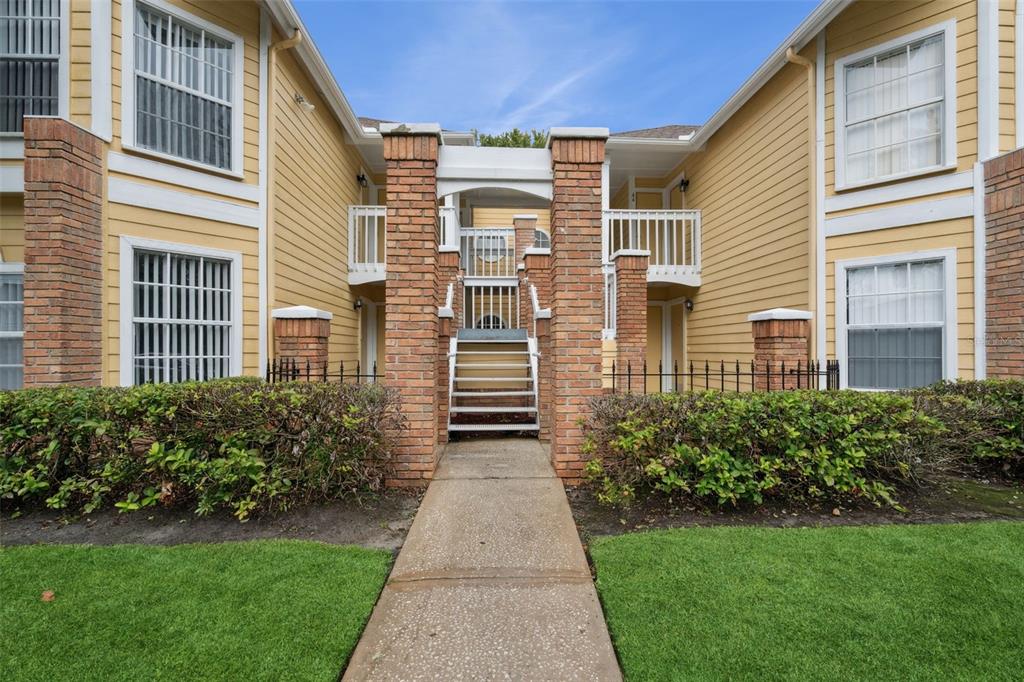 A concrete walkway leads to a set of stairs between two yellow apartment building sections — 2442 SWEETWATER CLUB CIRCLE UNIT 41, KISSIMMEE, FL