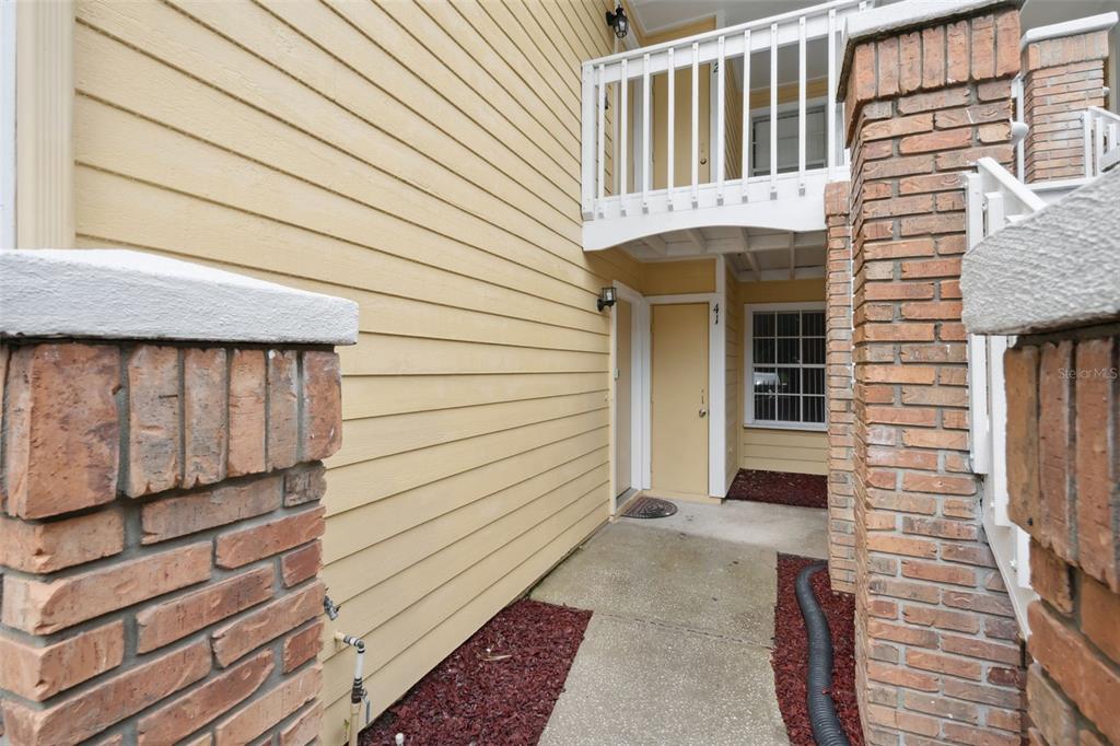 An exterior view of a building entrance with yellow siding, brick pillars, and a balcony — 2442 SWEETWATER CLUB CIRCLE UNIT 41, KISSIMMEE, FL