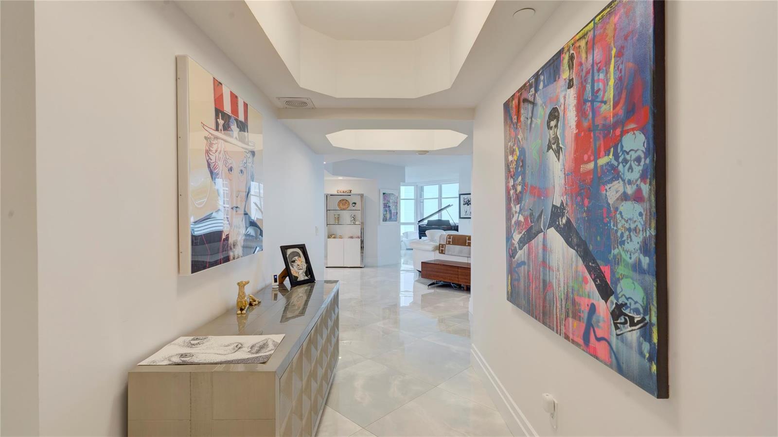 A hallway with marble floors, two large paintings, and a console table leads to a living area — 1440 S Ocean Boulevard # c, Pompano Beach FL 33062, POMPANO BEACH, FL