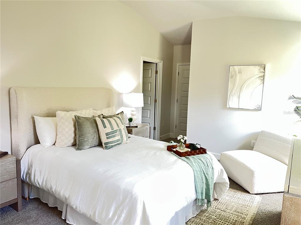 A bedroom features a queen bed with a textured headboard, a white chair, and neutral decor — 12964 KENT BRADLEY STREET, DADE CITY, FL