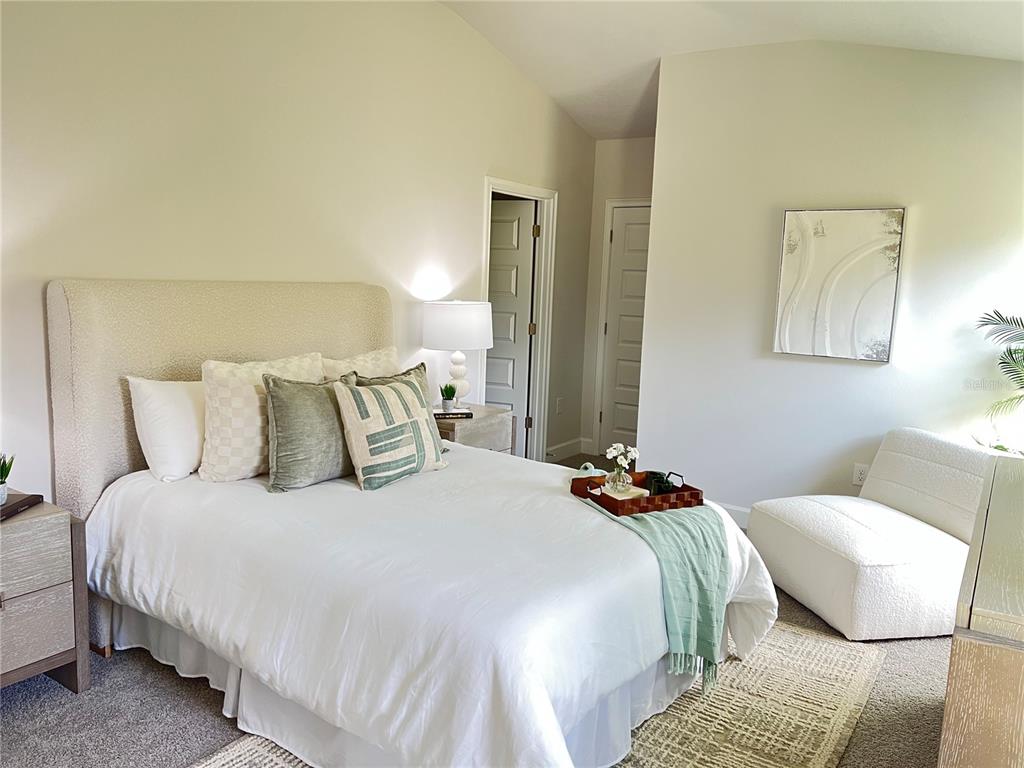 A bedroom features a queen bed with a textured headboard, neutral bedding, and a lounge chair — 12964 KENT BRADLEY STREET, DADE CITY, FL