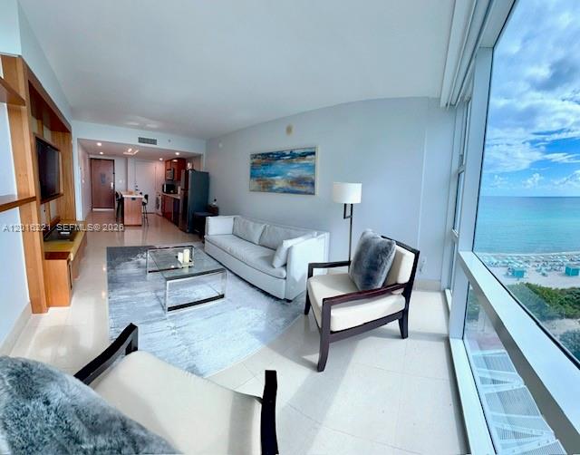 A modern living room features a sofa, accent chair, and floor-to-ceiling windows overlooking the ocean — 6801 Collins Ave, Miami Beach FL 33141, MIAMI BEACH, FL