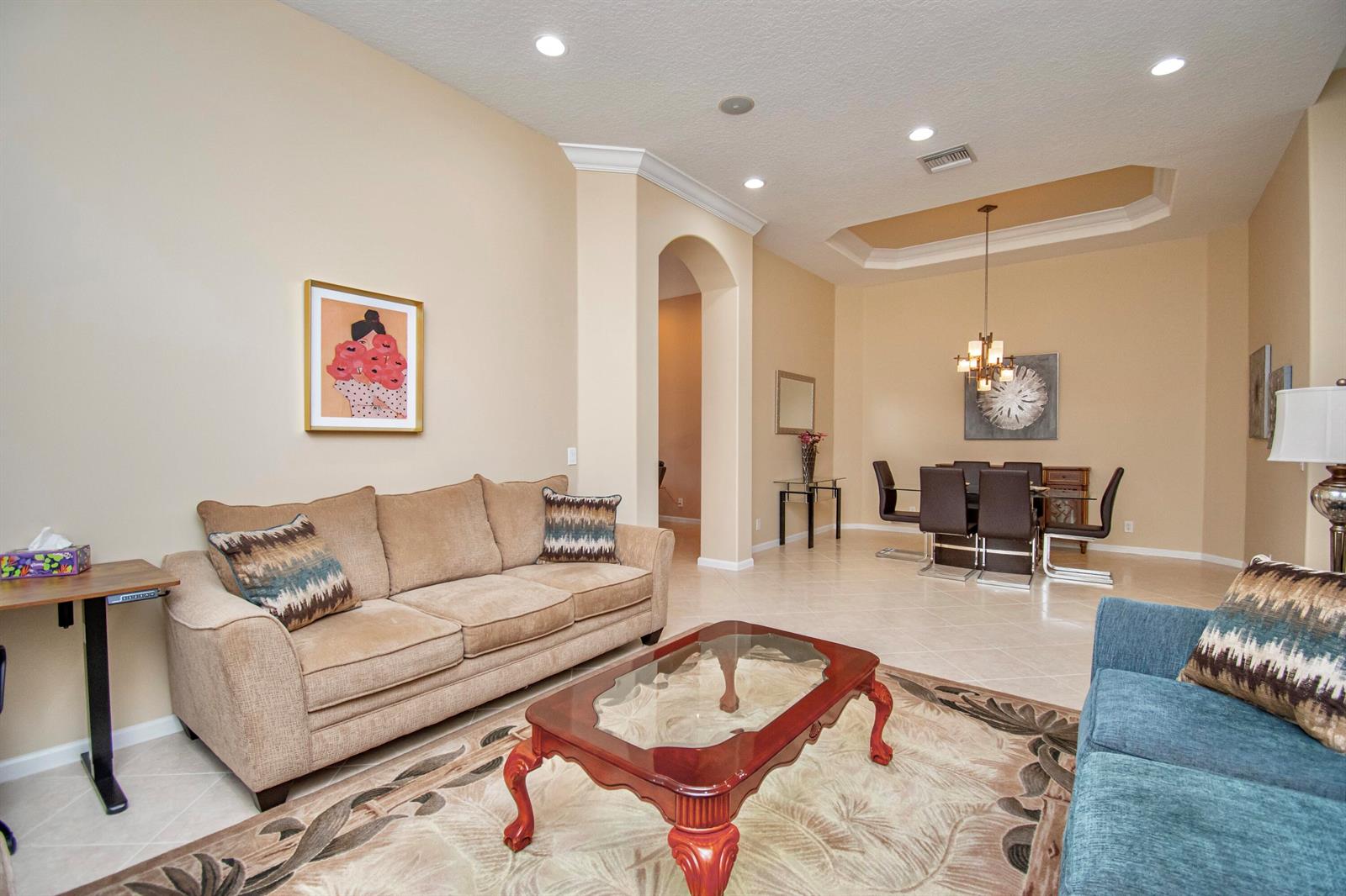 A living room with a beige sofa and blue loveseat opens to a dining area — 7080 Demedici Circle # 7080, Delray Beach FL 33446, DELRAY BEACH, FL