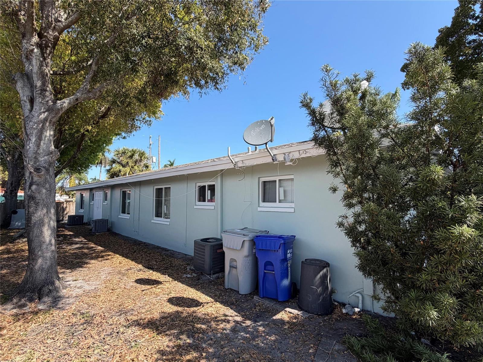 The exterior side of a light green house features windows, a satellite dish, and trash bins — 131 SW 14th Court, Pompano Beach FL 33060, POMPANO BEACH, FL