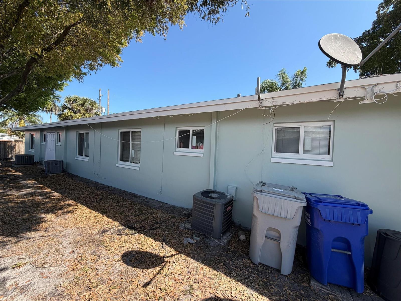 The exterior of a light green house features several windows, two air conditioning units, and trash bins — 131 SW 14th Court, Pompano Beach FL 33060, POMPANO BEACH, FL