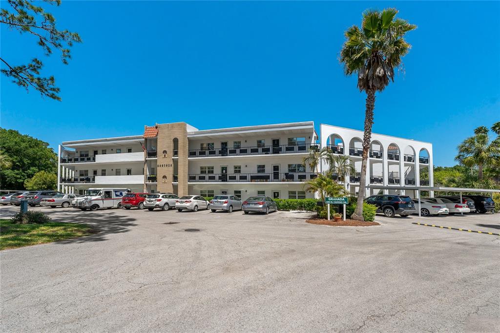 A three-story apartment building with a parking lot and a tall palm tree in front — 100 EL CAMINO DR UNIT 309, WINTER HAVEN, FL