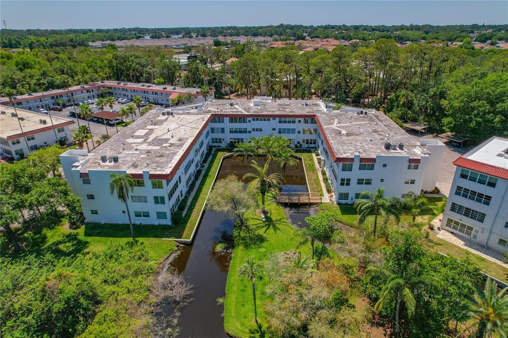 An aerial view shows a U-shaped apartment complex surrounding a central pond and green space — 100 EL CAMINO DR UNIT 309, WINTER HAVEN, FL