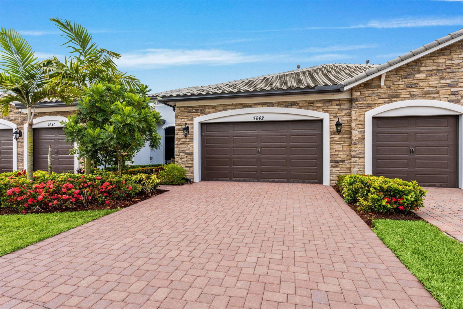 A paved driveway leads to the garage doors of a stone-faced residential building — 7642 N Blue Spring Drive, Parkland FL 33067, PARKLAND, FL