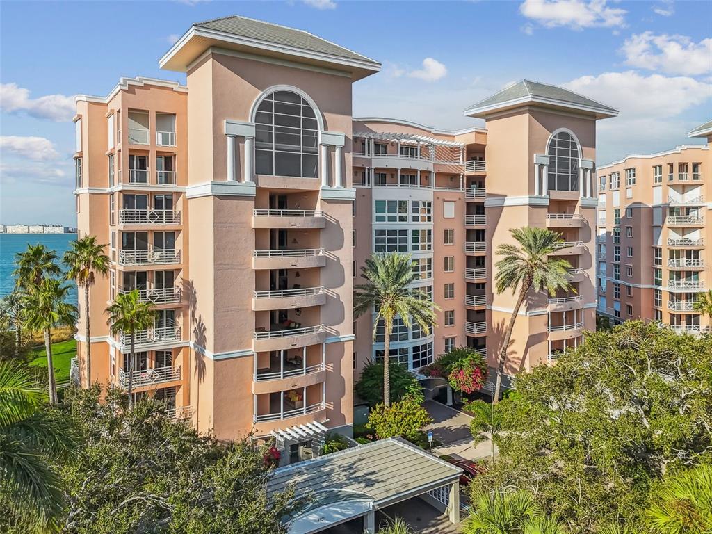 An exterior view of a multi-story peach-colored apartment building with balconies and palm trees — 4953 BACOPA LANE S UNIT 204, ST PETERSBURG, FL