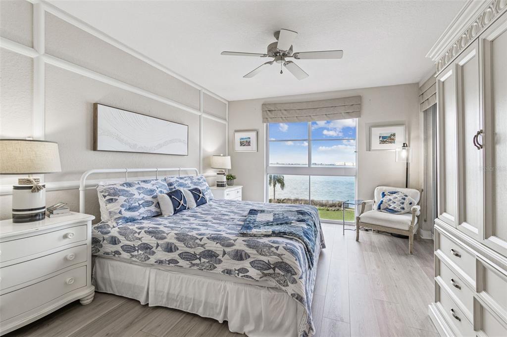 A bedroom features a coastal-themed bed, white furniture, and a large window overlooking the water — 4953 BACOPA LANE S UNIT 204, ST PETERSBURG, FL